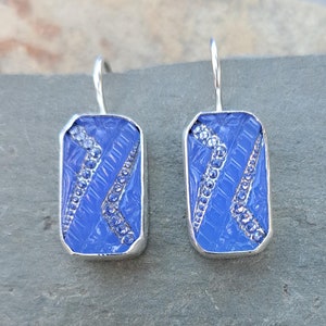 Puede incluir: Un par de pendientes de plata con un diseño de vidrio azul. El vidrio es texturizado y tiene un patrón geométrico con pequeños detalles plateados.