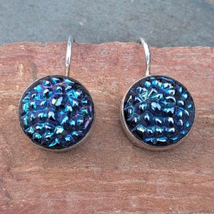 May include: A pair of silver dangle earrings with a round blue iridescent glass cabochon. The glass has a textured surface.