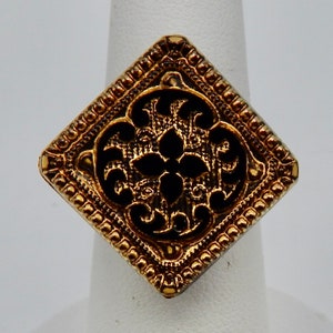 May include: A gold-toned ring with a square-shaped black enamel design featuring intricate floral patterns.