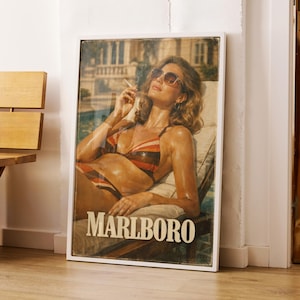 Puede incluir: Anuncio vintage de Marlboro enmarcado. La obra de arte muestra a una mujer en bikini y gafas de sol, sosteniendo un cigarrillo. La imagen está en un marco blanco. El anuncio tiene una estética retro y está apoyado contra una pared.
