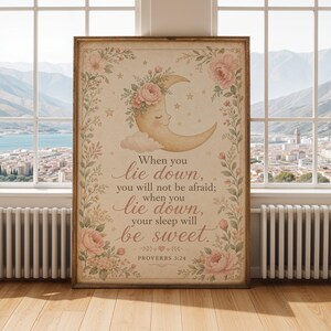 Può includere: Una stampa da parete rettangolare in cornice di legno raffigurante una luna crescente con un volto, accenti floreali rosa e il testo: When you lie down, you will not be afraid; when you lie down, your sleep will be sweet. PROVERBS 3:24.