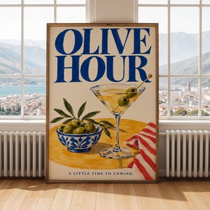 May include: A framed vertical poster featuring the text OLIVE HOUR at the top and A LITTLE TIME TO UNWIND at the bottom. The illustration shows a martini glass with two olives on a pick, a blue and white bowl of olives, and a red striped napkin.