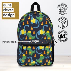 May include: Navy blue backpack featuring a playful dinosaur pattern with construction cones. The dinosaurs are in blue and green with yellow vests and hard hats. The backpack has a front pocket and a black handle. The text "Personalize it!" is visible.