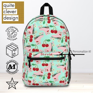 May include: A backpack with a light teal background featuring a pattern of pink roller skates and red cherries. The backpack has a black top handle and a front pocket with the name "Stevie" printed on it. The text "Personalize it!" is also visible.