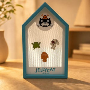 May include: A house-shaped display frame with a light blue border and a white honeycomb mesh centre. It features a black cat illustration at the top, a green frog, a brown rabbit, and a beige rabbit holding a red rose. The text JELLYCAT LONDON is printed at the bottom.