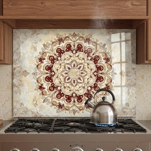 May include: A kitchen backsplash with a large, ornate mandala design in shades of red, cream, and gold. A stainless steel stove with a kettle on the burner is in front of the backsplash. Wooden cabinets frame the scene.