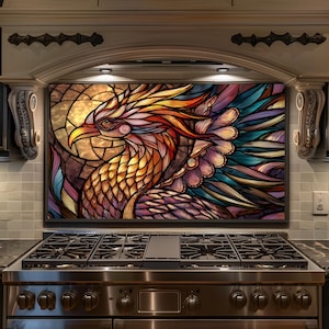 May include: A colorful stained-glass style phoenix design, featuring shades of orange, red, yellow, and blue. The artwork is framed and mounted above a stainless steel gas range in a kitchen setting. The phoenix is the focal point.