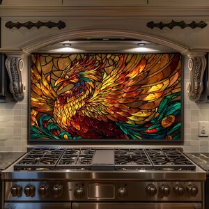 May include: A stained glass panel depicting a phoenix with outstretched wings, in shades of red, orange, yellow, and green. The artwork is set above a stainless steel gas range in a kitchen setting.