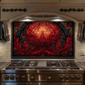 May include: A vibrant, stained-glass style backsplash featuring a fiery red phoenix design. The artwork is framed in black and set above a stainless steel gas range. The phoenix has a detailed, feathered appearance with shades of red, orange, and yellow.