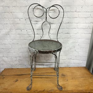 May include: A vintage metal chair with a green painted seat and a scrolled back. The chair is made of twisted metal and has a distressed finish.