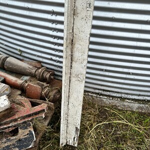 May include: A weathered white wooden board with a rough texture and chipped paint. The board is leaning against a metal surface.