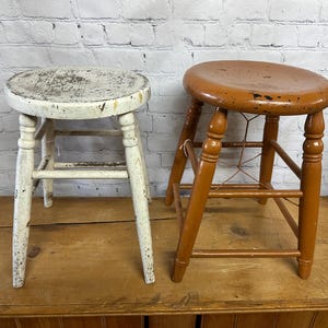 May include: Two wooden stools, one white and one brown, with a distressed finish. The stools are sitting on a wooden surface.