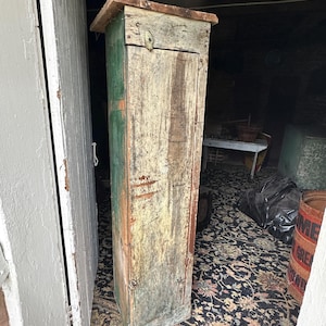 May include: A tall, narrow, wooden cabinet with a single door. The cabinet is painted in shades of green, white, and brown, and has a distressed, antique look. The door has a simple, metal handle.