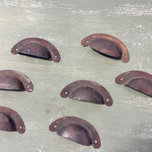 May include: Eight antique-style metal drawer pulls in a rusty brown color. The pulls are shaped like half-circles with a slight curve in the center.