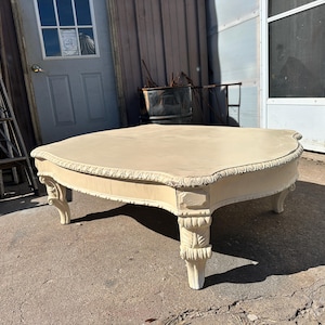 May include: A white painted coffee table with ornate carvings on the legs and a scalloped edge on the top.