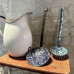 May include: A white enamel pitcher with a black handle, a blue and white enamel ladle, and a blue and white enamel strainer on a wooden surface.