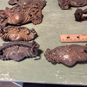 May include: A collection of antique, ornate, metal drawer pulls in various styles. The pulls are made of a dark, aged metal with intricate details and are in various sizes.