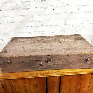 May include: A rectangular wooden storage chest with a weathered, muted brown finish. The box features a hinged lid, three metal latches along the front edge, and visible signs of wear, including surface scratches and areas of paint loss.