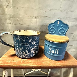 May include: Blue and white enamelware mug and salt shaker with a wooden lid. The salt shaker has the word "Salt" written on it.