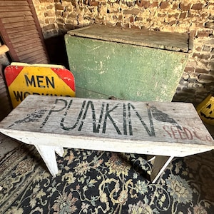 May include: A white wooden bench with the words "PUNKIN SEEDS" painted in black on the top. The bench is sitting on a black and white patterned rug.