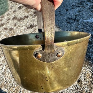 May include: A brass pot with a wooden handle. The pot has a worn, aged look and is likely antique.