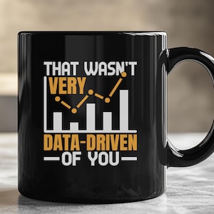 May include: Black ceramic mug with a white and gold graphic. The text on the mug reads "THAT WASN'T VERY DATA-DRIVEN OF YOU" with a bar graph design. The mug has a curved handle.