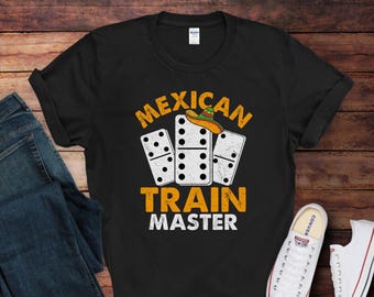 May include: Black t-shirt with the text "MEXICAN TRAIN MASTER" in yellow and white. The design includes three dominoes and a sombrero. A pair of blue jeans and white sneakers are visible in the image.