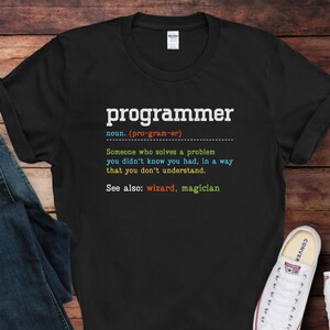 May include: Black t-shirt with the word "programmer" in white, followed by a definition. The definition is in multiple colors. The shirt is paired with blue jeans and white sneakers.