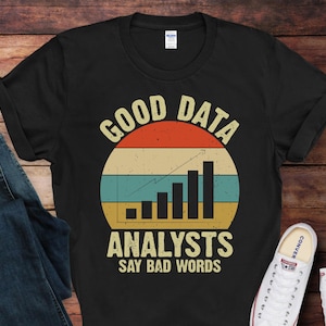 May include: Black t-shirt with a vintage-style graphic that says "Good Data Analysts Say Bad Words". The graphic features a bar chart with an upward trend and a retro color scheme.