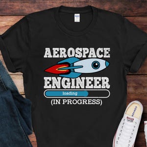 May include: Black t-shirt with a white graphic of a rocket ship and the text "Aerospace Engineer (In Progress)" with a loading bar.