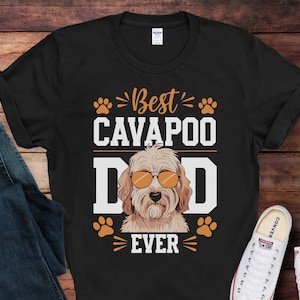 May include: Black t-shirt with white text that reads "Best Cavapoo Dad Ever". The shirt features a cartoon image of a Cavapoo dog wearing sunglasses.