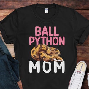 May include: Black t-shirt with a pink graphic of a ball python snake and the text "Ball Python Mom".