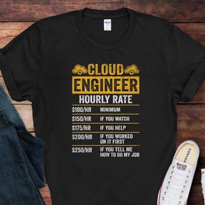 May include: Black t-shirt with the text "CLOUD ENGINEER HOURLY RATE" in yellow and white. The shirt lists hourly rates from $100 to $250 based on the level of involvement. A pair of blue jeans and white sneakers are visible.