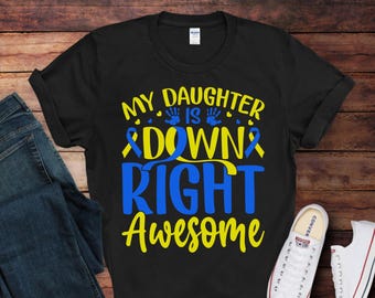 May include: Black t-shirt with the text "My daughter is down right awesome" in yellow and blue lettering. The text is surrounded by yellow and blue ribbon symbols and handprints.