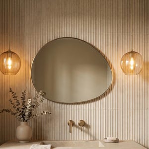 May include: A modern bathroom vanity with a stone countertop and a wooden cabinet. A large, irregularly shaped mirror hangs above the sink, with two globe pendant lights on either side. The wall has a vertical ribbed design.
