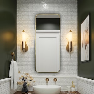 May include: A modern bathroom with a white vessel sink, gold fixtures, and a dark wood vanity. The walls are tiled with small white tiles, and the mirror has a gold frame. Decorative sconces flank the mirror, and a towel hangs on a gold ring.