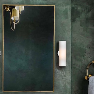 Puede incluir: Un tocador de baño con una encimera de mármol blanco con vetas marrones. La encimera tiene un grifo dorado, un lavabo de porcelana blanca y un espejo con marco dorado encima. Hay dos apliques de pared dorados con pantallas de vidrio blanco a cada lado del espejo.