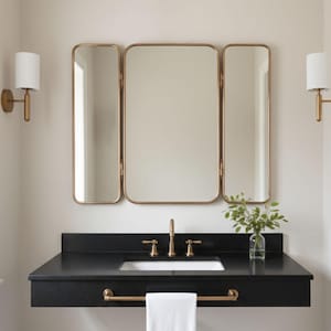 Può includere: Un mobile da bagno moderno con piano nero e specchio a tre ante con cornice dorata. Il mobile ha un lavandino bianco, un rubinetto dorato e un portasciugamani dorato. Due applique dorate affiancano lo specchio.