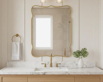 Puede incluir: Un mueble de baño con un espejo con marco dorado, una encimera blanca y un mueble de madera. El espejo tiene una forma curva única. Un toallero dorado sostiene una toalla blanca. Un grifo dorado y dos lámparas están montados encima del espejo.