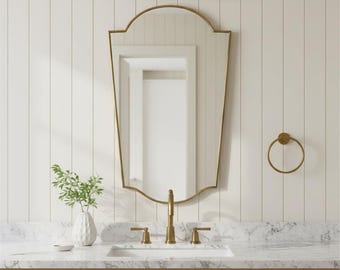 Puede incluir: Un juego de tocador de baño con espejo, grifo y lámpara dorados. El espejo tiene una parte superior arqueada y está montado sobre una encimera de mármol. También se ven un lavabo blanco y un pequeño jarrón con vegetación.