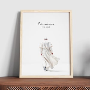 Può includere: Una stampa incorniciata di una fotografia in bianco e nero di Papa Francesco che si allontana dalla telecamera. Il testo "Francis 1936 - 2025" è stampato sotto l'immagine.