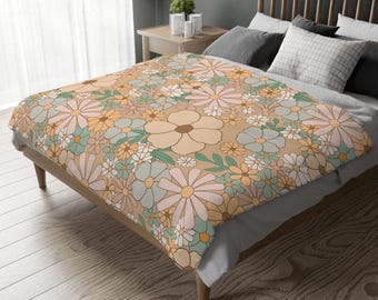 Könnte beinhalten: Eine floral gemusterte Decke mit Retro-Design. Die Decke zeigt ein sich wiederholendes Muster aus großen und kleinen Blumen in Pfirsich-, Rosa-, Blau- und Weißtönen auf einem beigen Hintergrund. Die Decke liegt auf einem hölzernen Bettrahmen.
