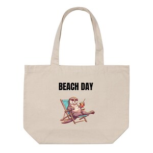 Peut inclure: Un sac fourre-tout en toile beige orné d'une illustration représentant une loutre portant des lunettes de soleil, assise sur une chaise de plage bleue avec une boisson. Le texte BEACH DAY est imprimé en lettres capitales noires au-dessus.