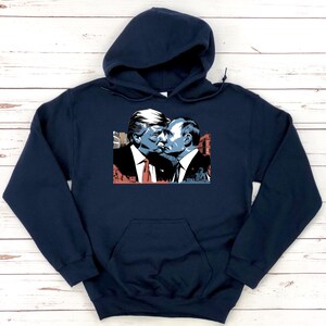 May include: A navy blue hooded sweatshirt with a graphic print of two men kissing. The men are depicted in a cartoon style and are wearing suits. The graphic is in a blue, red, and white color scheme.