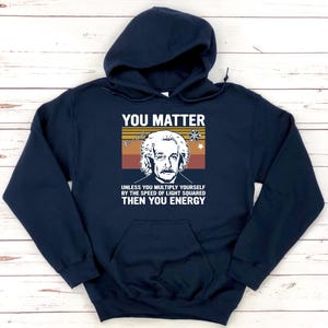 May include: Navy blue hooded sweatshirt with a front graphic featuring Albert Einstein and the text "YOU MATTER." Below the image, the text reads, "UNLESS YOU MULTIPLY YOURSELF BY THE SPEED OF LIGHT SQUARED THEN YOU ENERGY."