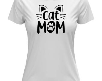 Puede incluir: Camiseta blanca con un gráfico negro. El gráfico presenta orejas de gato, bigotes, las palabras "Cat Mom" y una huella de pata. La camiseta tiene mangas cortas y cuello redondo.