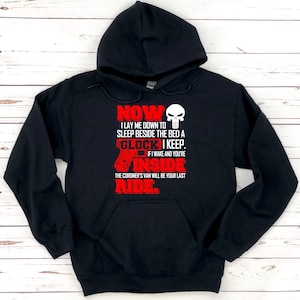 May include: Black hooded sweatshirt with the text "NOW I LAY ME DOWN TO SLEEP BESIDE THE BED A GLOCK I KEEP. IF I WAKE AND YOU'RE INSIDE THE CORONER'S VAN WILL BE YOUR LAST RIDE." Features a white skull graphic.