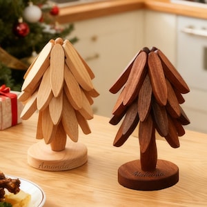 Peut inclure: Décorations en bois en forme de sapins de Noël, dans des tons marron clair et foncé. Un arbre est marron clair avec le nom "Amanda" gravé sur la base. L'autre est marron foncé avec le nom "Makayla" gravé. Un pot blanc avec un couvercle est tenu.