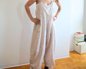 May include: White linen overalls with paint splatters. The overalls have adjustable straps and a loose fit. The model is wearing red sneakers.