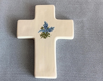 Puede incluir: Una cruz de cerámica blanca con un diseño floral azul y verde. Las flores son estilizadas y se asemejan a las campanillas azules.